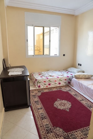 A bedroom with two beds, a desk, a window, and a patterned rug.