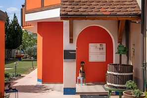 A building with a red facade, a tiled roof, and a small outdoor seating area with a table and chairs.