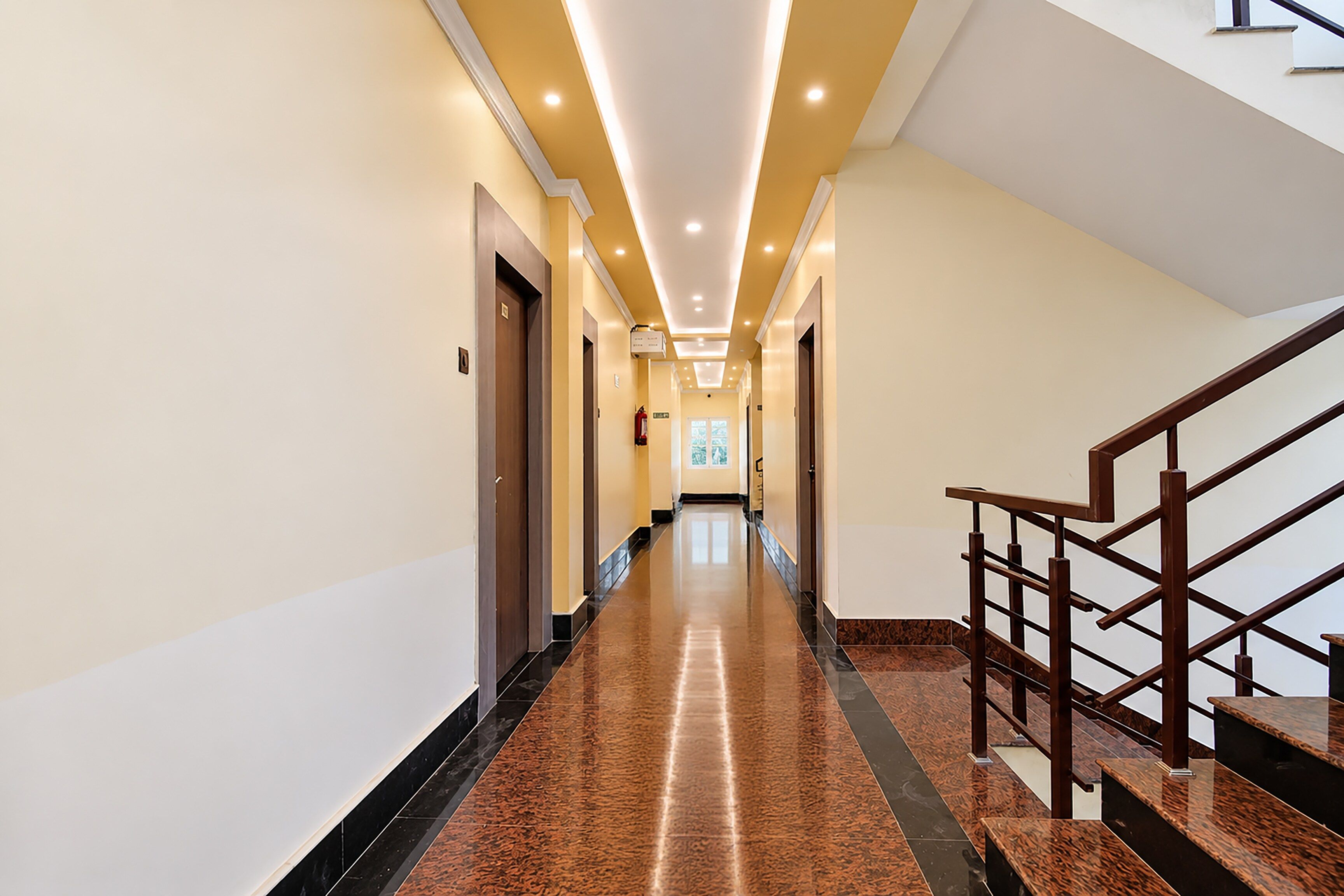 A hotel hallway with a marble floor, wooden doors, and a staircase with a wooden railing.