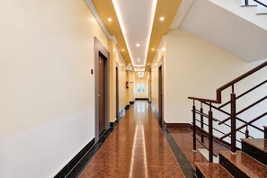 A hotel hallway with a marble floor, wooden doors, and a staircase with a wooden railing.