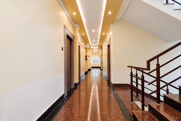 A hotel hallway with a marble floor, wooden doors, and a staircase with a wooden railing.