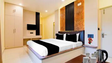 Quarto de hotel com cama, mesa de cabeceira, televisão, guarda-roupa e espaço para café.