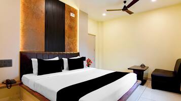 Habitación de hotel con una cama grande, una mesita de noche, una silla, un ventilador de techo y una lámpara fijada a la pared.