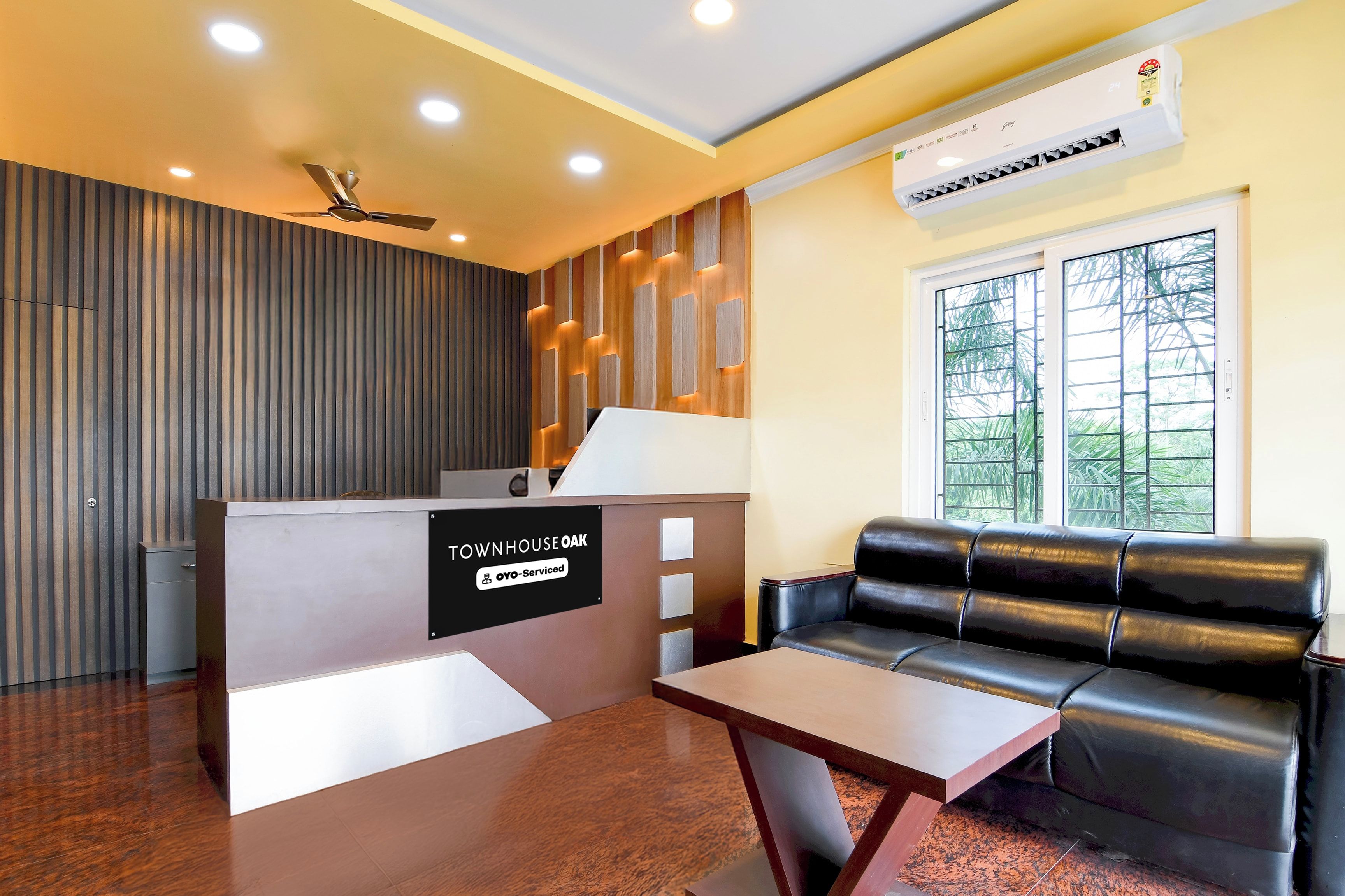 A reception area with a reception desk, a leather sofa, a small table, and a window with a view of greenery.