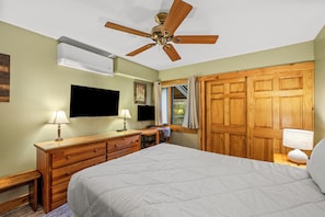 Une chambre à coucher comprenant un lit, une commode en bois, un ventilateur de plafond, un téléviseur fixé au mur et une armoire en bois.