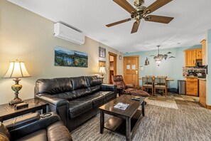 A living room with a leather sofa, a coffee table, a ceiling fan, and a kitchen area with wooden cabinets. - Ski, Soak & Snuggle | Ski-In/Out + Fireplace (Steamboat Springs)
