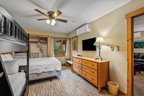 Una habitación de hotel con cama, escritorio, televisor, ventilador de techo y aire acondicionado.