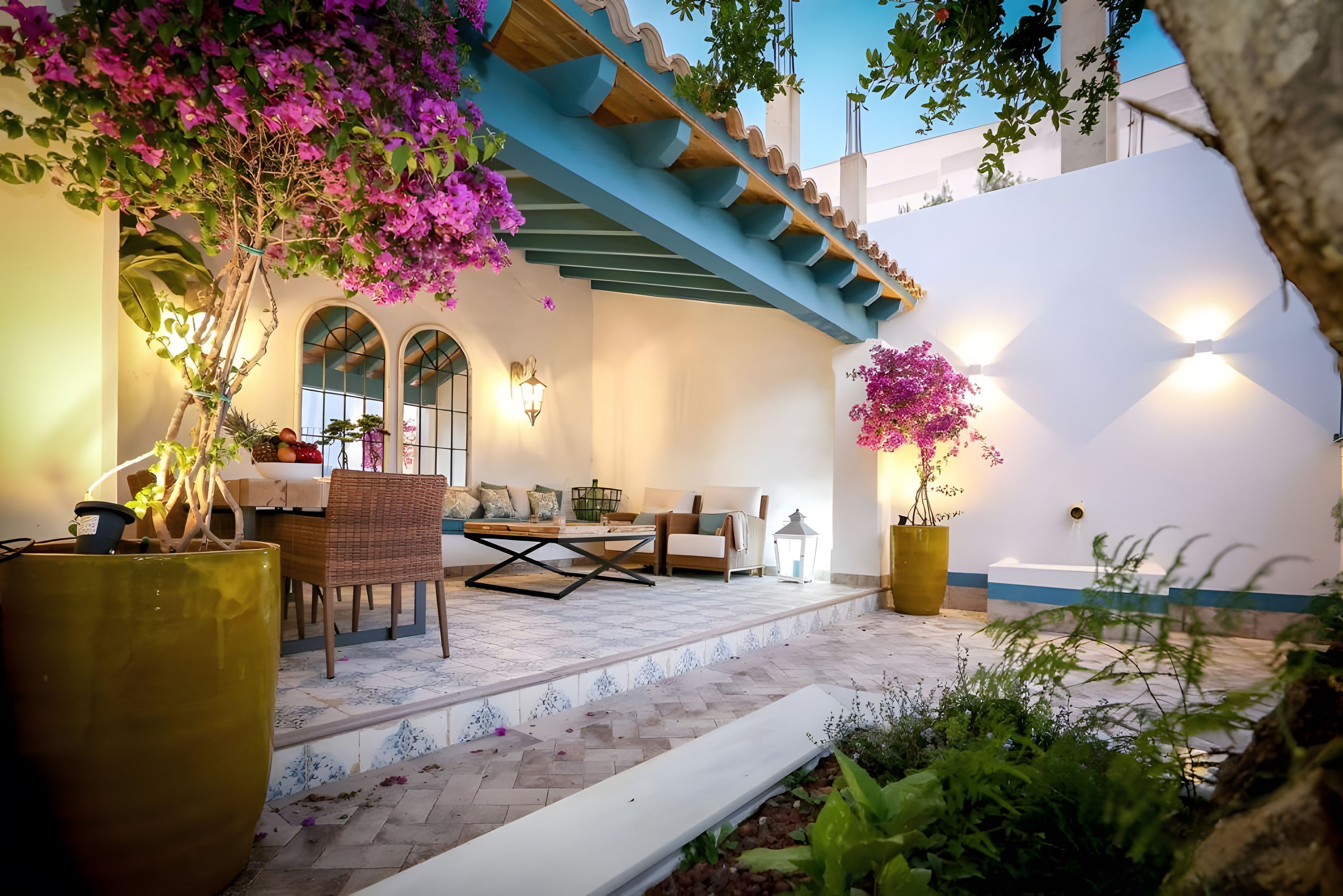 Un espace extérieur accueillant, aménagé avec une table et des chaises, entouré de plantes en pot et bordé d’un mur blanc.
