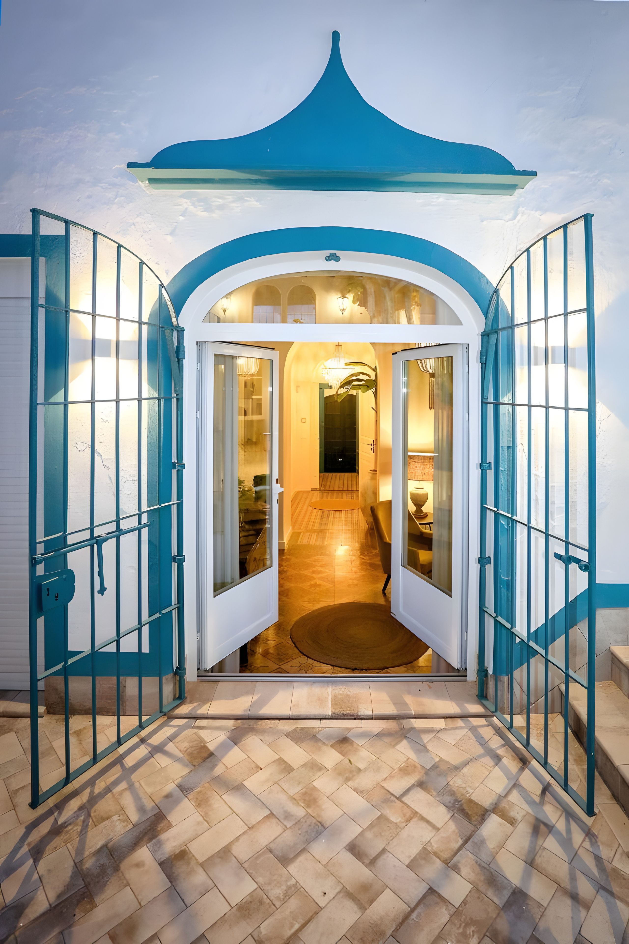 Une entrée fermée par un portail mène à un bâtiment dont le sol est recouvert de carreaux, et qui offre une vue sur l’intérieur.