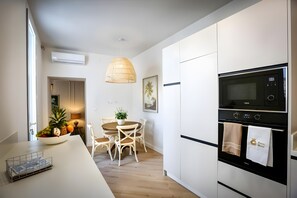 A modern kitchen with white cabinetry, a built-in oven, and a dining area with a table and chairs.