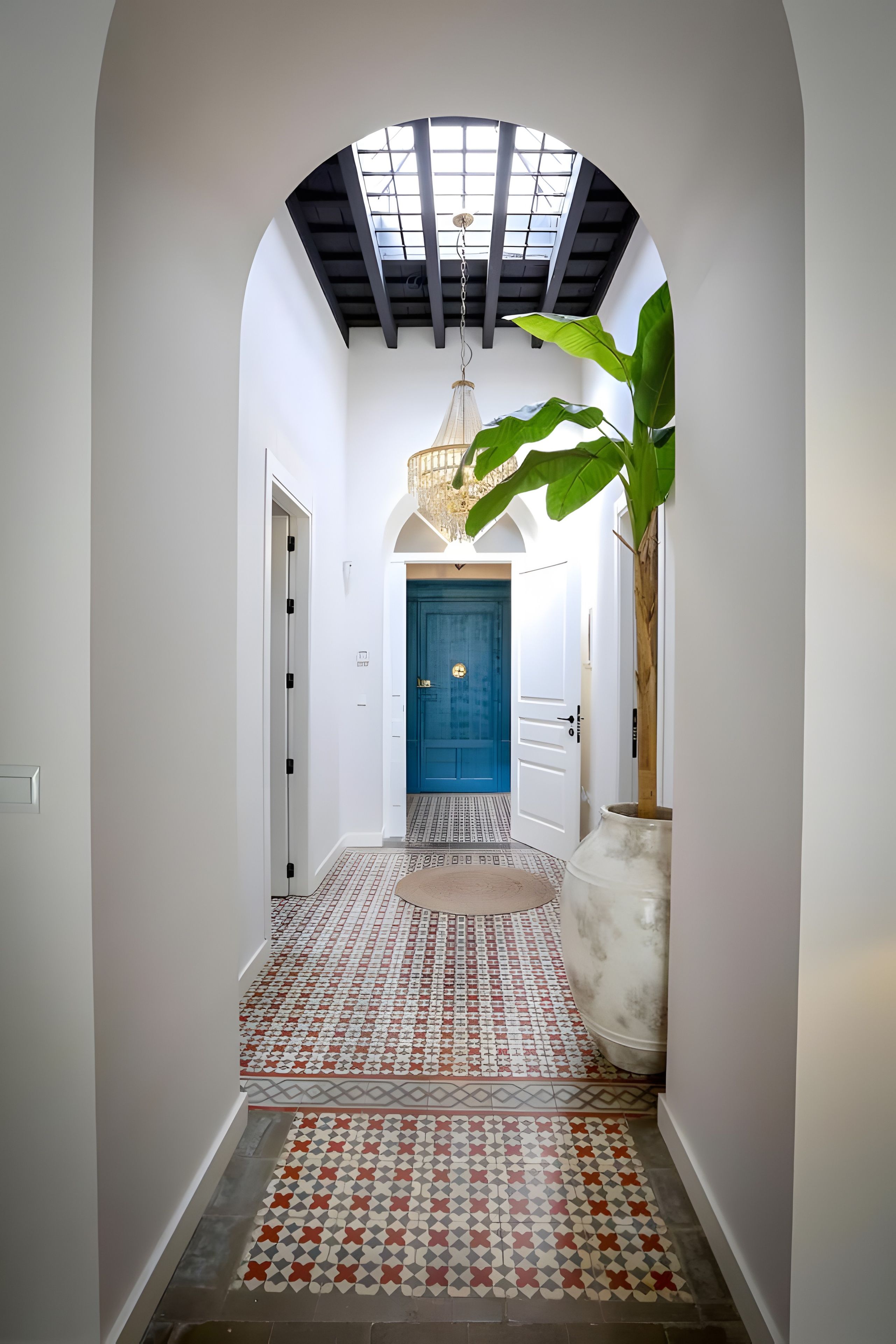 Un couloir avec un sol à motifs, une porte bleue et une plante.