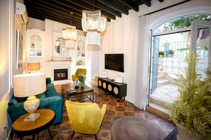 A living room with a fireplace, sofa, armchair, coffee table, TV, and a view of the outside.