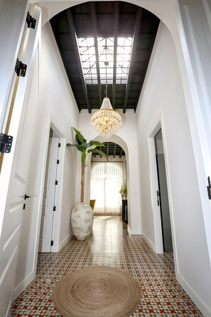 A hallway with a patterned floor, a large vase, and a hanging chandelier.