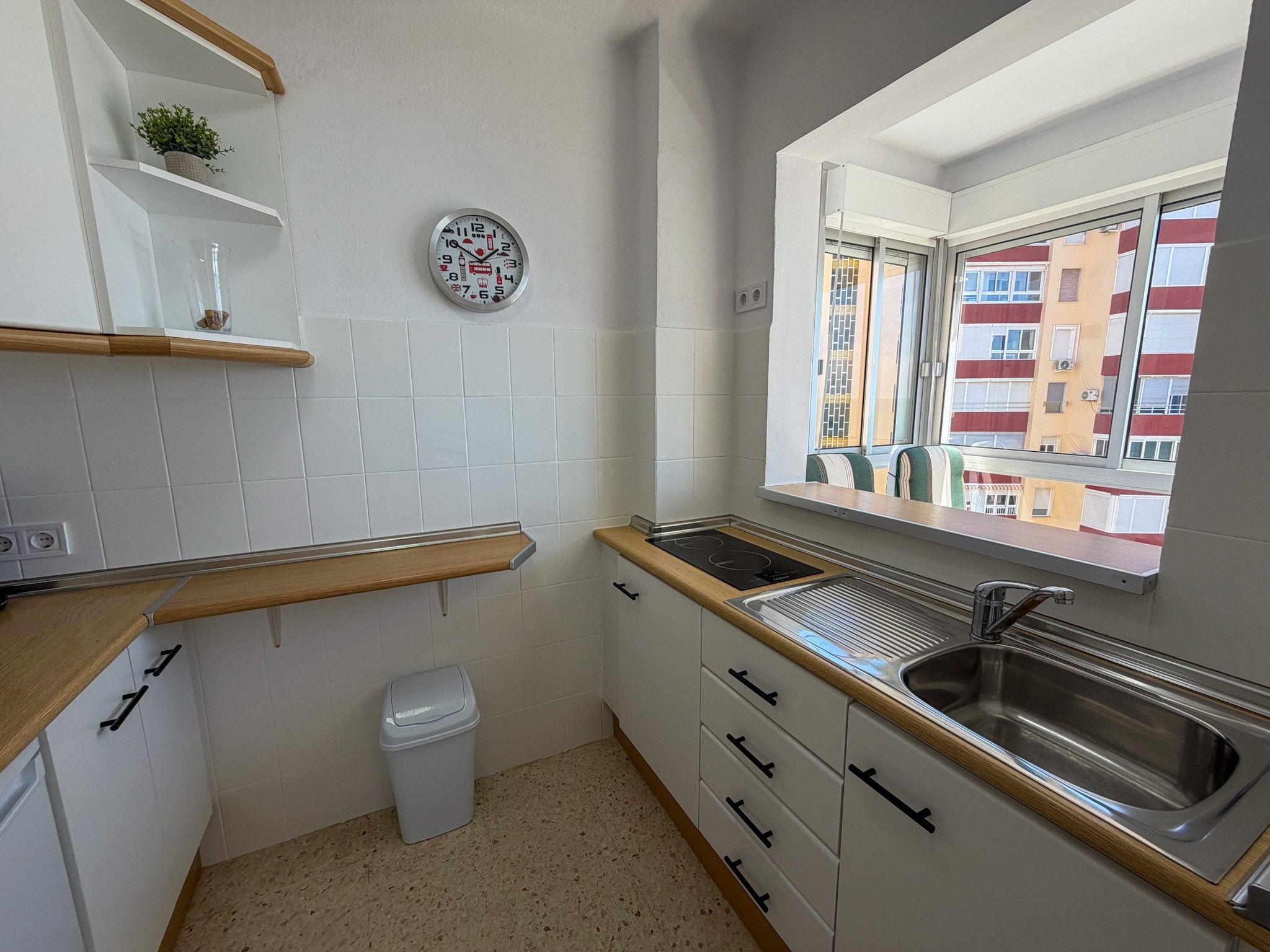 Una cucina compatta con mobili bianchi, un lavello in acciaio inossidabile e una finestra con vista sugli edifici.