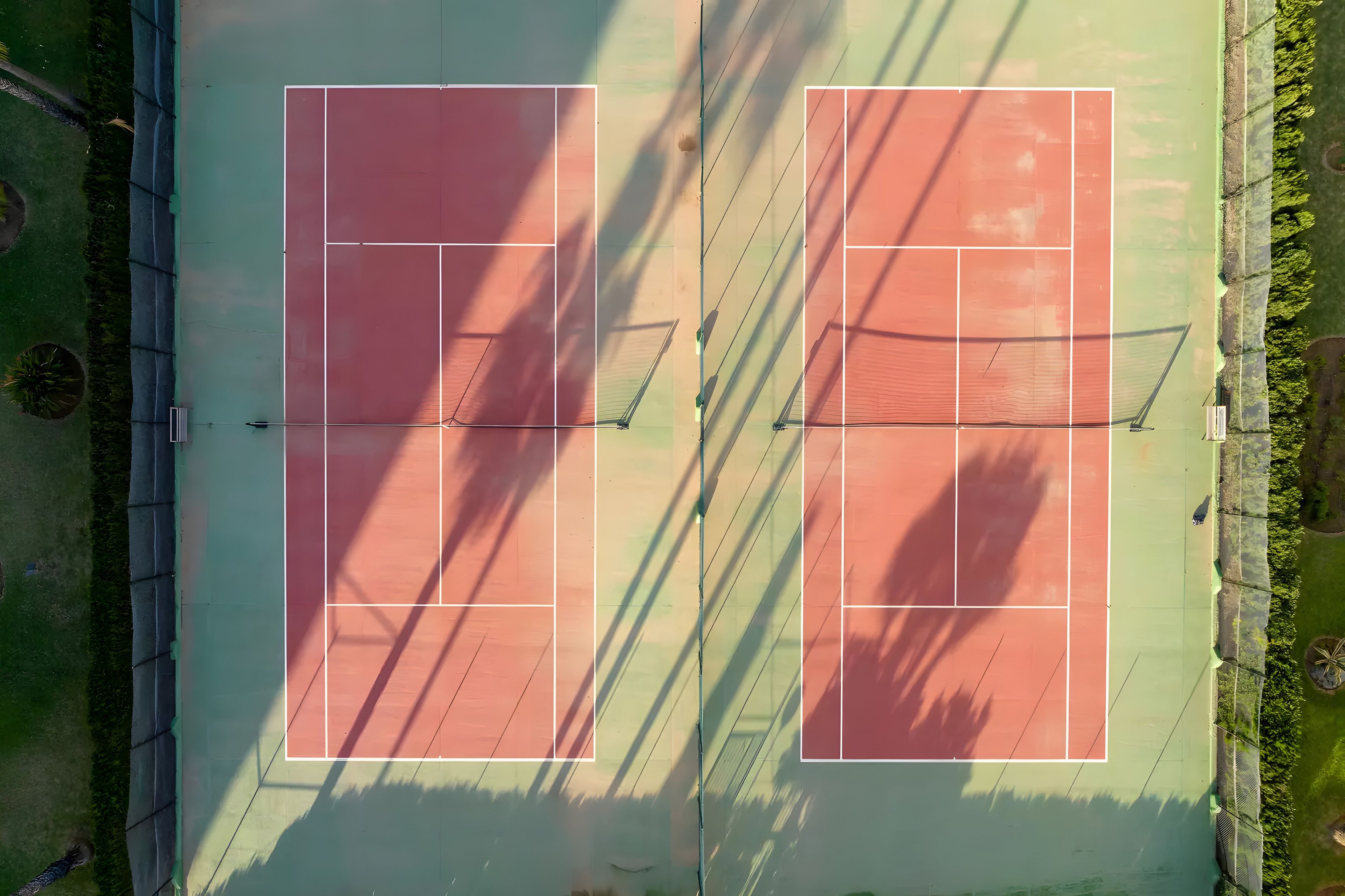 An aerial view of a tennis court with a net, surrounded by greenery.