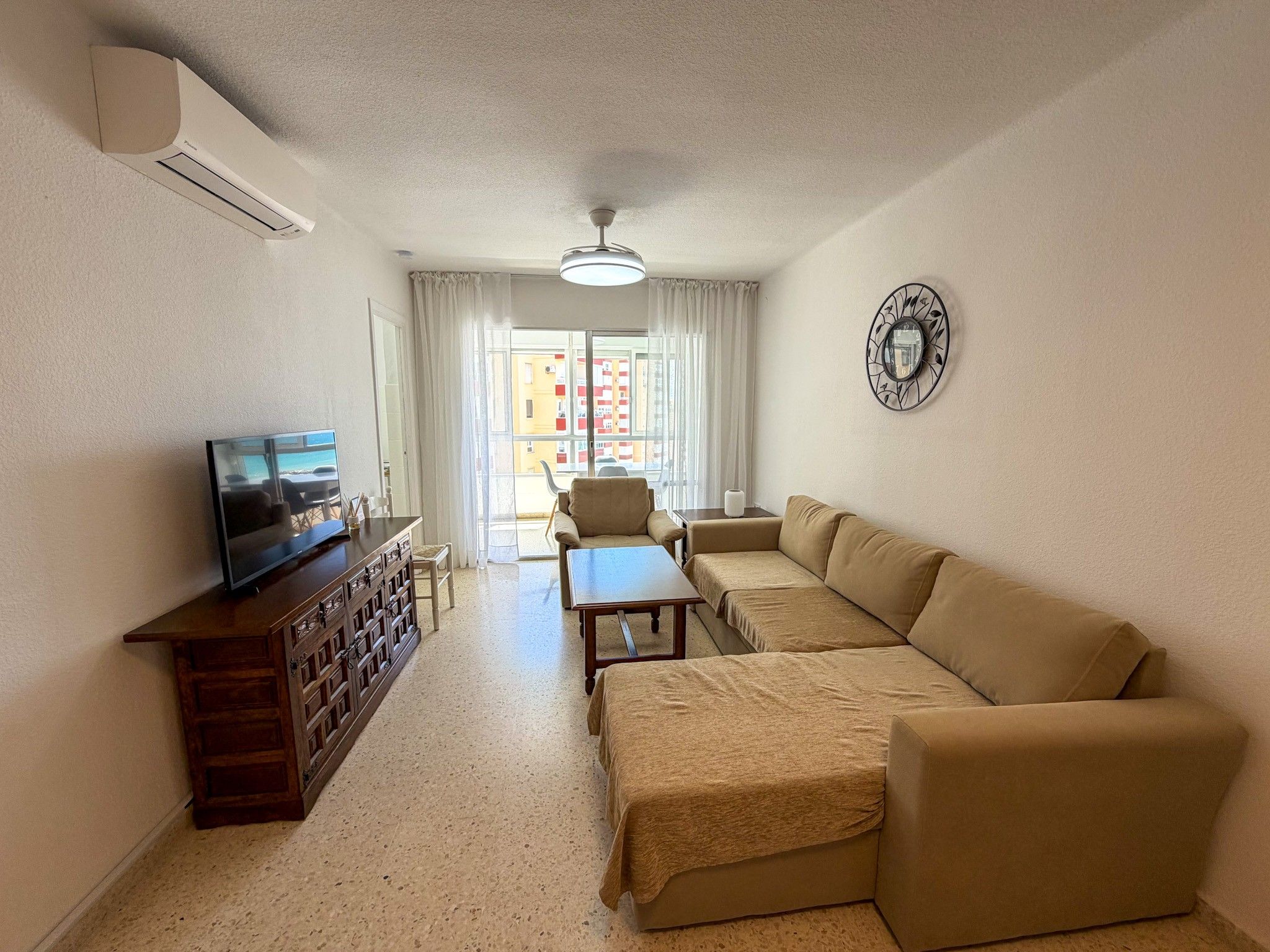 A living room with a sofa set, a television, a wooden cabinet, and a decorative wall clock.