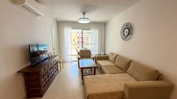 A living room with a sofa set, a television, a wooden cabinet, and a decorative wall clock.