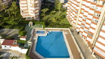 A high-rise residential building with a rooftop pool, surrounding greenery, and a clear view of the surrounding area.
