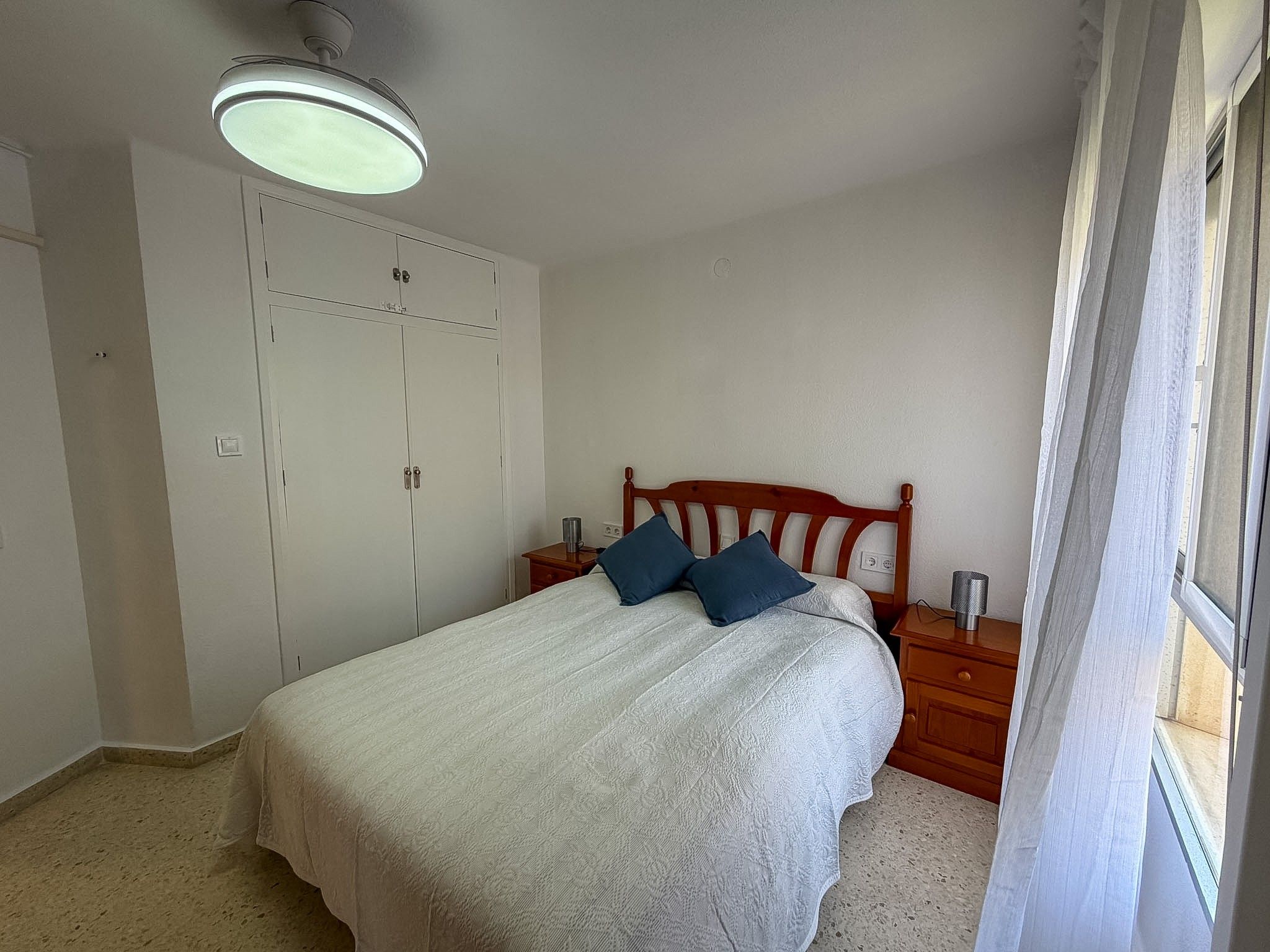 Een slaapkamer met een bed, een kledingkast, een nachtkastje en een raam.