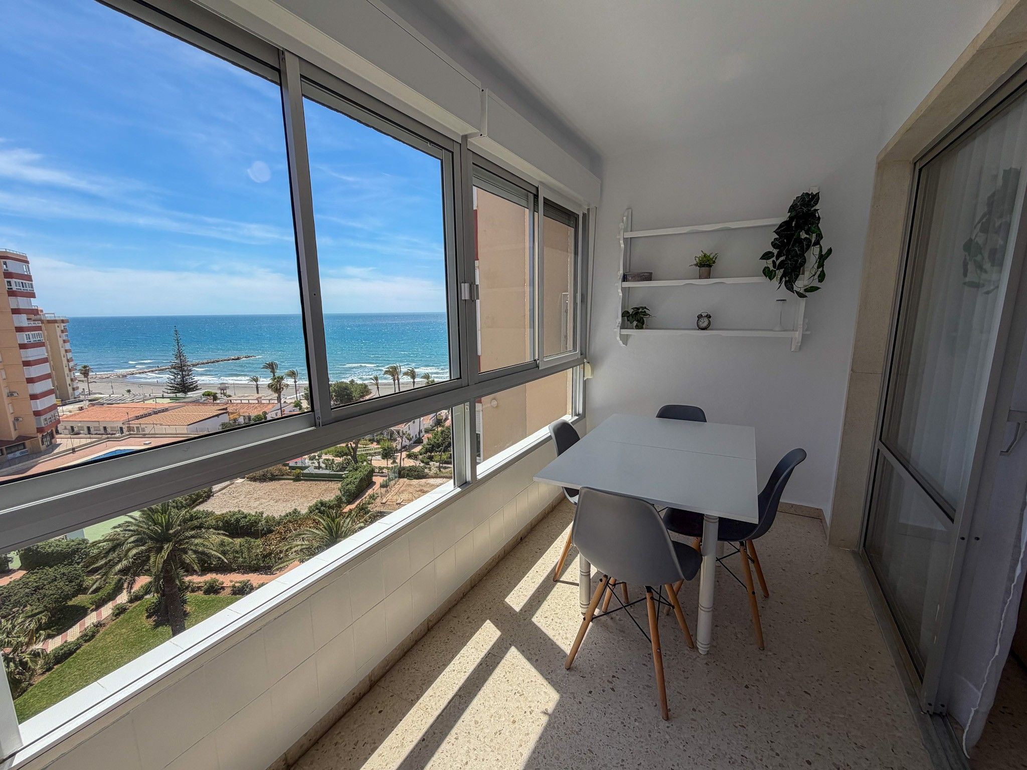 A balcony with a table and chairs, overlooking a beach and ocean.