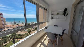 A balcony with a table and chairs, overlooking a beach and ocean.