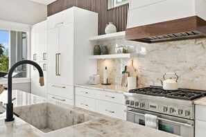 A modern kitchen with white cabinetry, a stainless steel stove, and marble countertops. - Luxury Home - Close to Beach -Saltwater Pool & Spa (Naples)