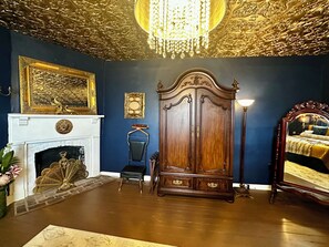 Ein Zimmer mit Kamin, einem großen, verzierten Bett, einem Kleiderschrank und einer Chandelüster.