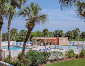 A pool area with lounge chairs and umbrellas, surrounded by palm trees and a building with a covered seating area. - St. Augustine Beach & Tennis Club - Unit 213 (Saint Augustine)