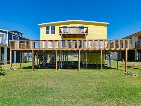 A two-story yellow house with a wooden deck and a balcony. - Passing Winds | Deck, Community Pool, + Near Beach (Galveston)