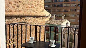 A balcony with a stone wall, a table with two chairs, and a view of neighboring buildings.