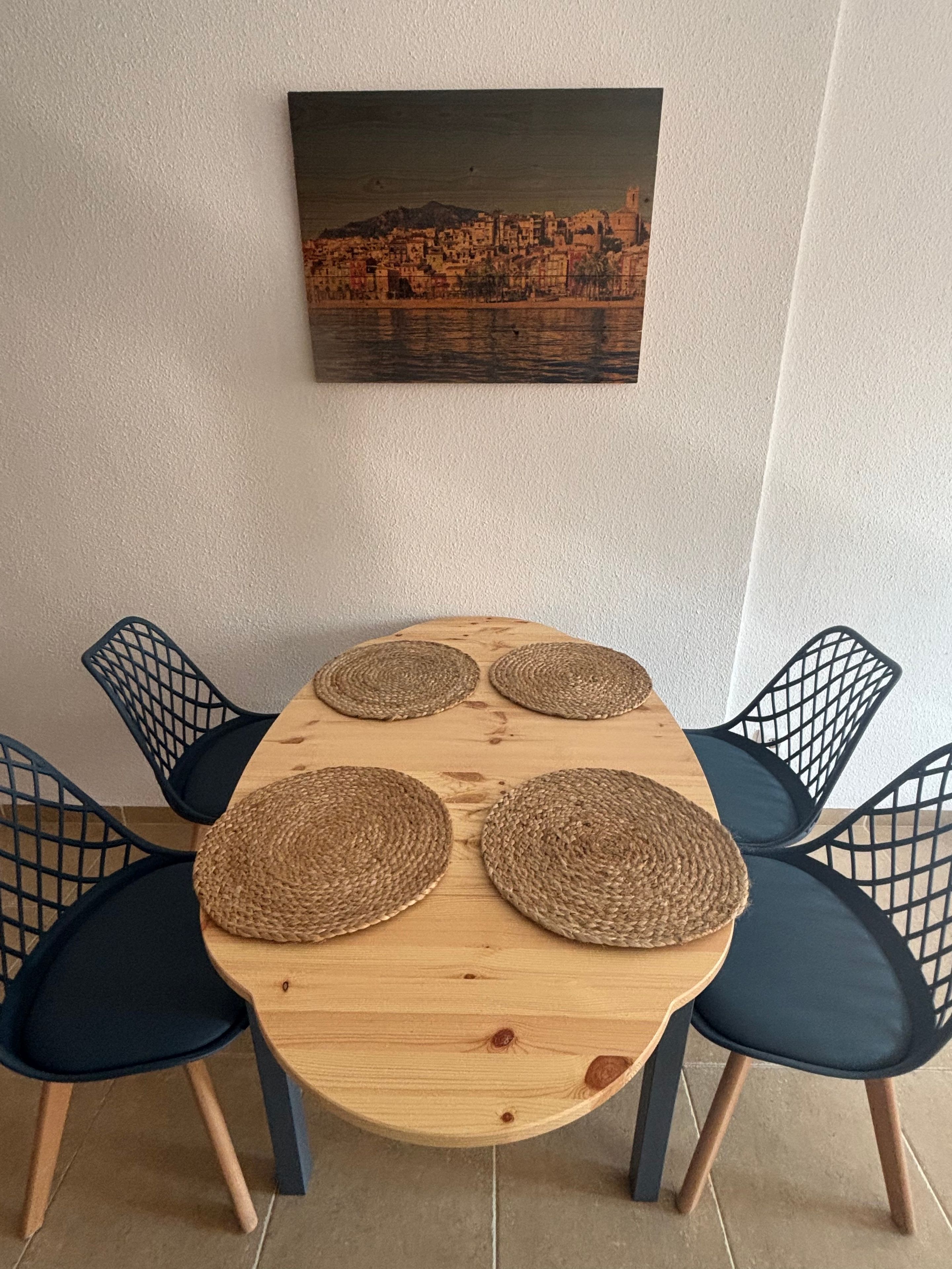 A dining table with four woven placemats, surrounded by four dark chairs with a grid-like backrest.