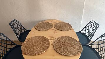 A dining table with four woven placemats, surrounded by four dark chairs with a grid-like backrest.