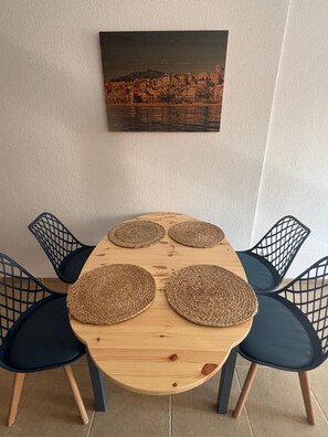 Une table à manger agrémentée de quatre sets de table en fibres tressées, entourée de quatre chaises sombres dont le dossier est constitué d’un motif en réseau.