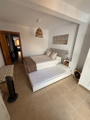 Een slaapkamer met een bed, nachtkastje, lamp en een ventilator.