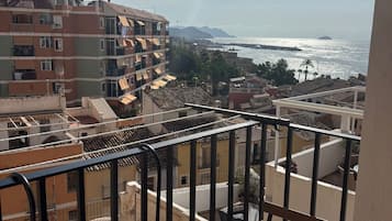 A balcony with a table, a cup, and a view of the sea and buildings.