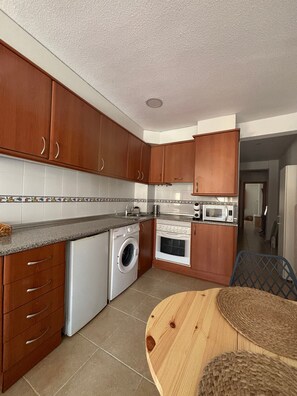 Een kleine keuken met houten kastjes, een wasmachine, een oven en een magnetron.