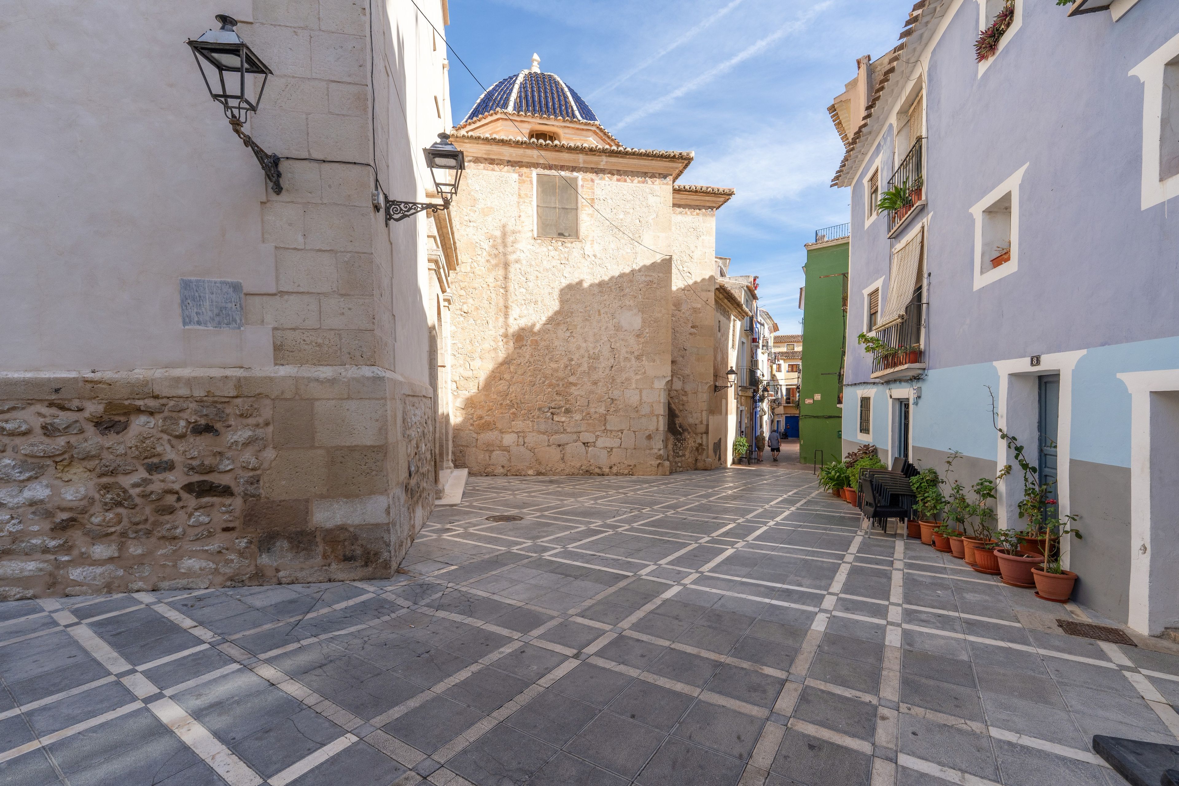 A narrow street with stone buildings, a tiled pavement, and a small dome structure in the distance.