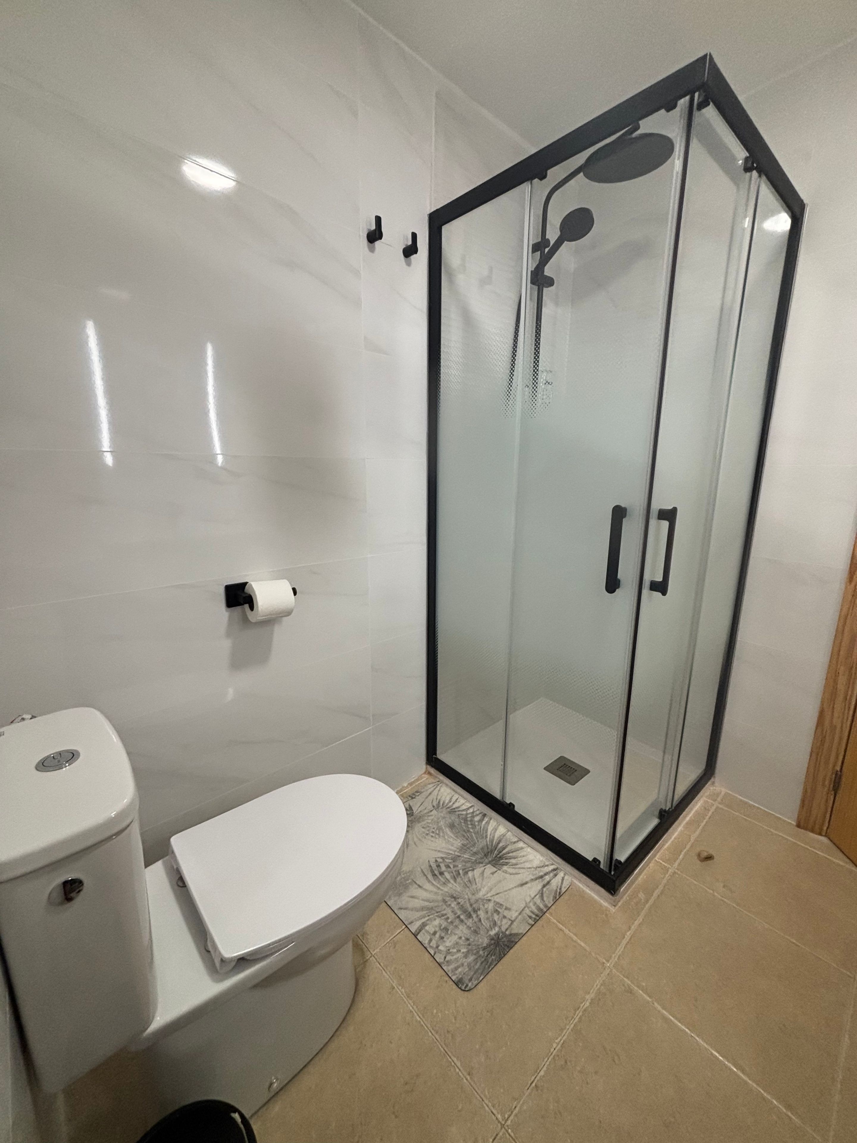 Un baño con inodoro, ducha con cerramiento de vidrio y un felpudo estampado.