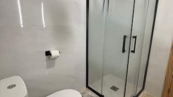 Un baño con inodoro, ducha con cerramiento de vidrio y un felpudo estampado.