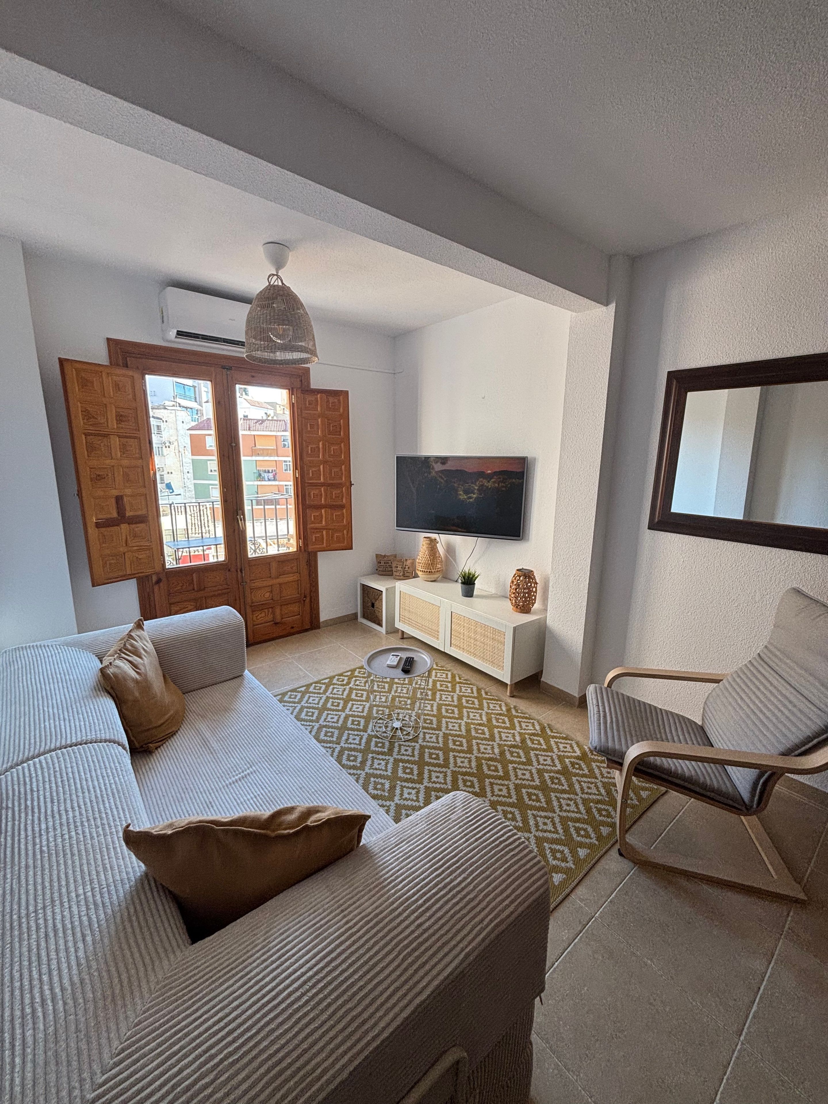 Una sala de estar con un sofá, un sill ón, un televisor y una alfombra estampada.