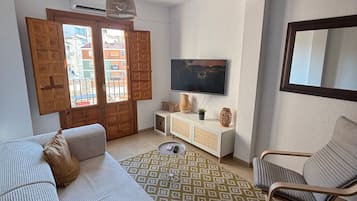 Una sala de estar con un sofá, un sillón, un televisor y una alfombra estampada.
