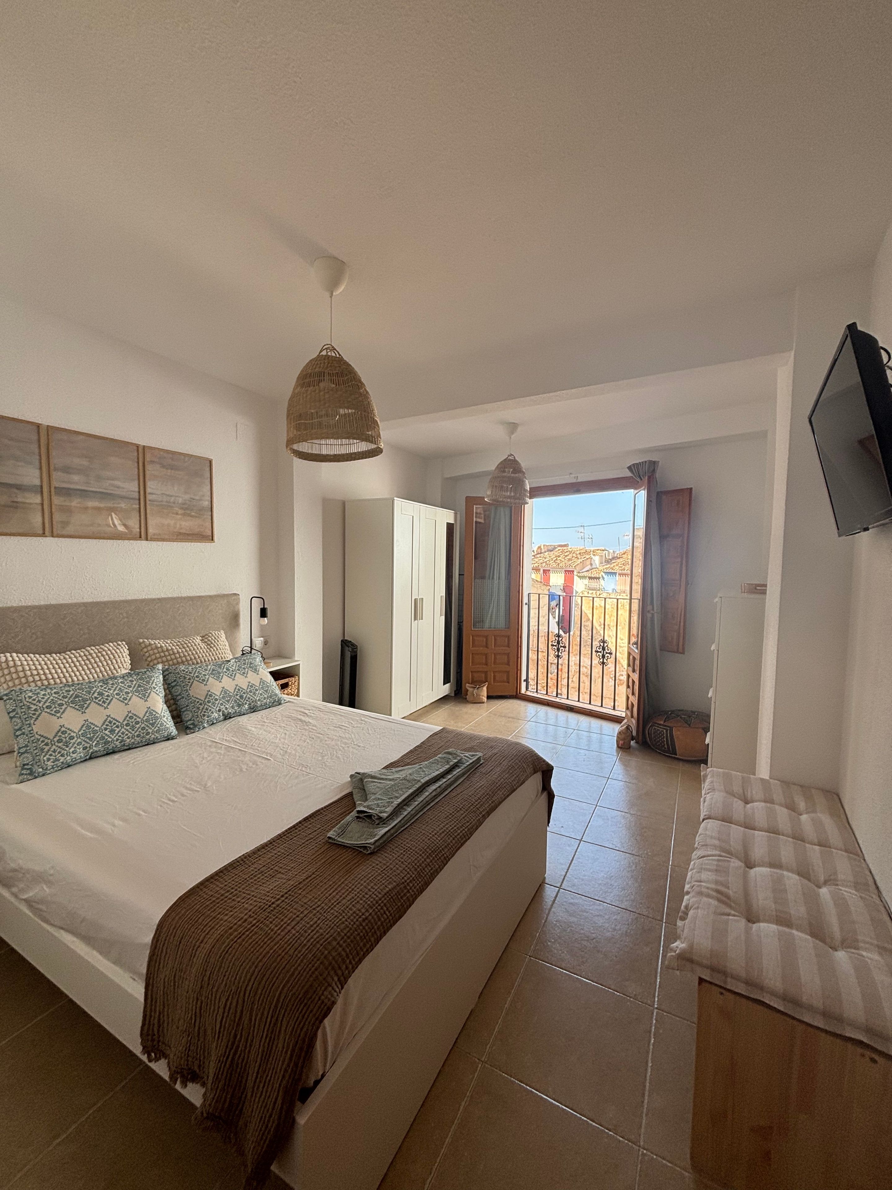 A bedroom with a bed, bedside table, and a view of the outside.