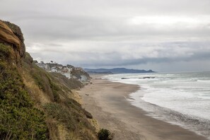 A coastal beach with houses on a cliff, a sandy shore, and the ocean. - Olivia Beach Beauty; Hot Tub, Grill, Near Beach Access (Lincoln City)