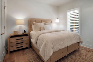 A bedroom with a wooden bed, bedside lamps, a nightstand with drawers, and a window with blinds.