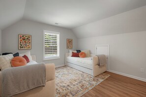 A room with a white ceiling, a large window with blinds, a white sofa with cushions, a patterned rug, and a door.