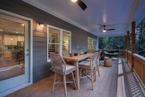 A covered outdoor dining area with a table and chairs, a ceiling fan, and a view of the surrounding trees.