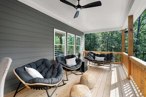 A covered porch with two rocking chairs, a ceiling fan, and a view of the surrounding trees.