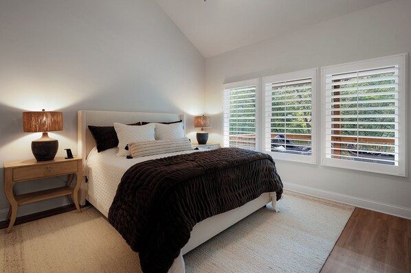 A bedroom with a bed, two bedside tables, a nightstand, and a window with blinds.