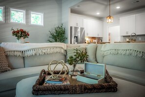 Un salon moderne avec un canapé, une table basse agrémentée d’objets décoratifs et une vue sur la cuisine.