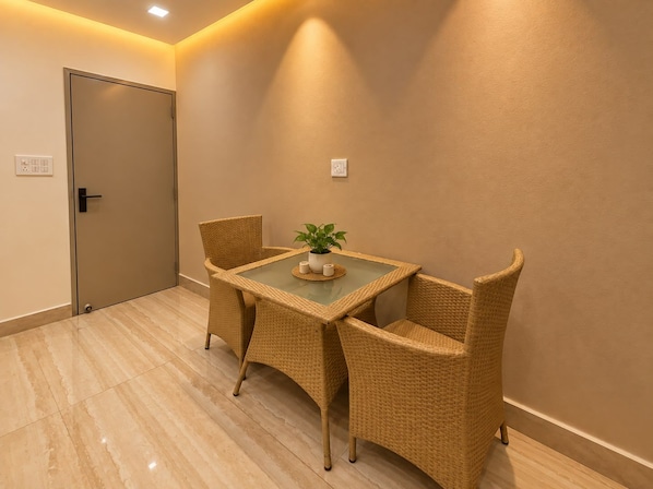 A room with a glass-top table, wicker chairs, a potted plant, and a door.